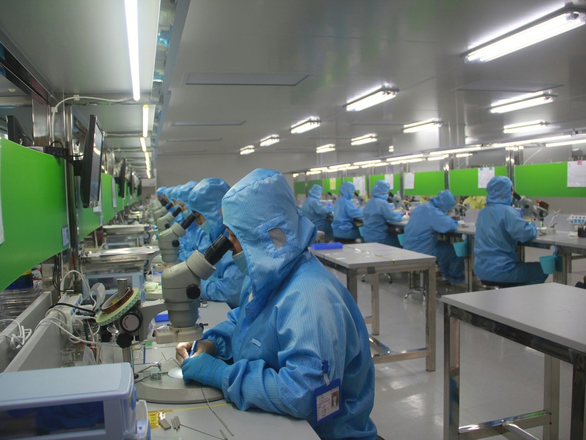 Technicians in protective suits assembling medical devices in a clean room